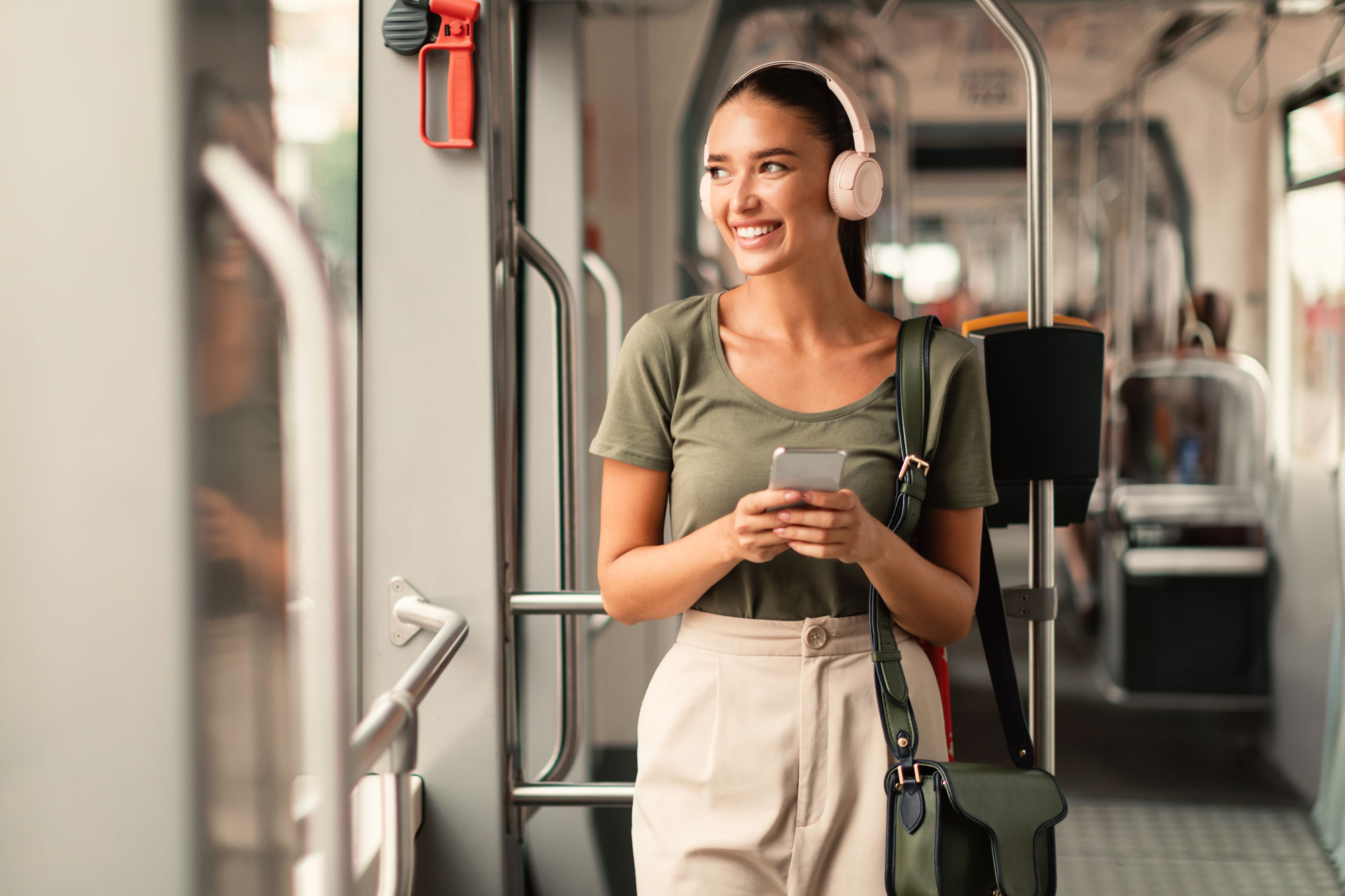 Junge Frau steht entspannt grinsend in der Bahn und hört Musik über Ihr Handy auf Bluetooth Kopfhörer